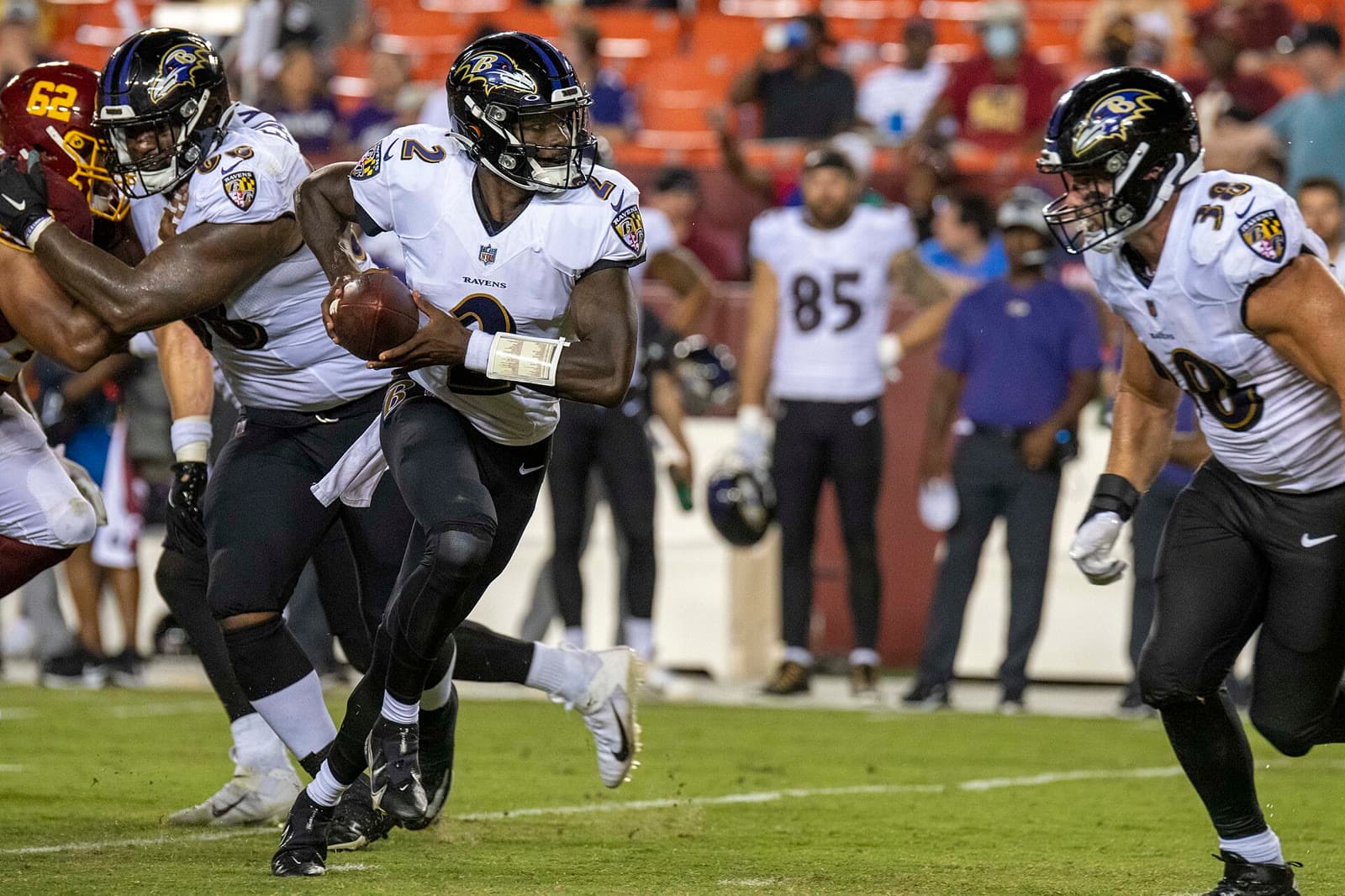 Tyler Huntley, No. 2 in a white Ravens uniform, runs out of the pocket with the ball tucked as his linemen block.