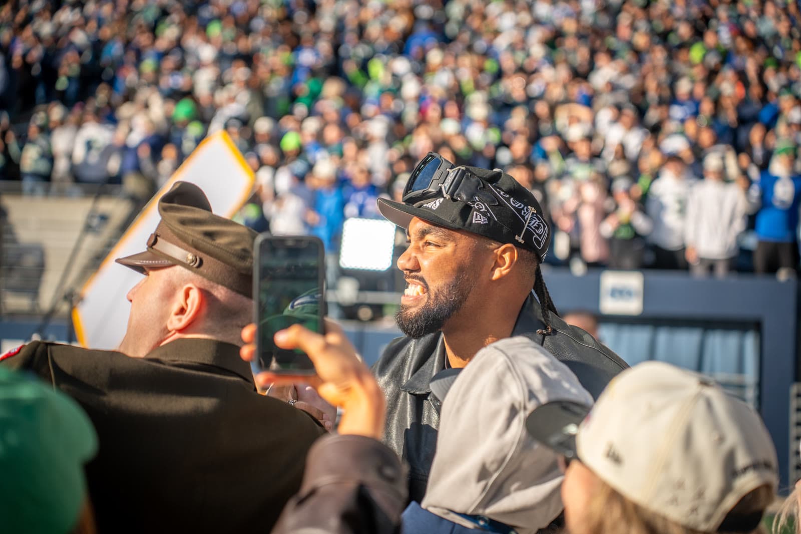 Leonard Williams, in a black cap and goggles, grins in a crowd of fans holding up phones in front of packed stands.