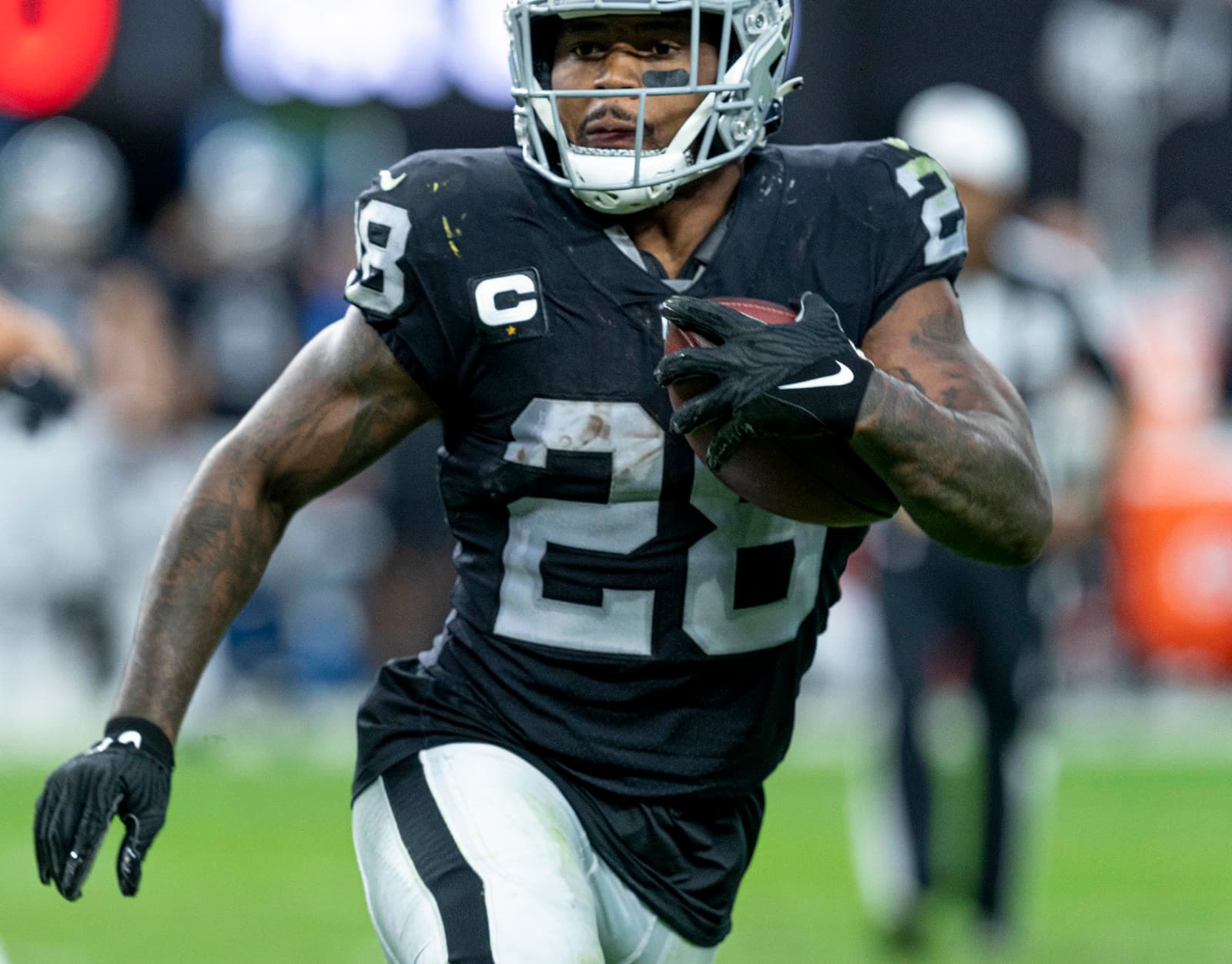Josh Jacobs in a black Raiders jersey carries the ball during a game against Washington.